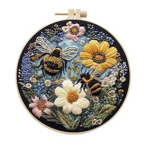 May include: Embroidered hoop art featuring a detailed floral and bee design. The artwork showcases a black background with colorful flowers, including yellow sunflowers, pink and white daisies, and blue wildflowers. Two bees are prominently displayed.