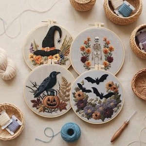 May include: Four circular embroidery hoops on light fabric featuring Halloween designs: a black witch hat with flowers, a skeleton surrounded by orange and purple flowers, a black crow perched on a pumpkin, and three black bats above autumn flowers.