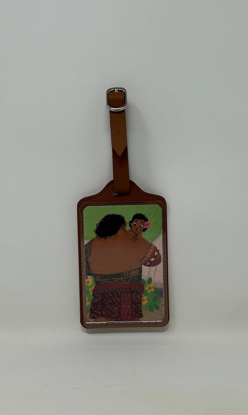 Pode incluir: Uma etiqueta de bagagem com uma al&ccedil;a e fivela de couro marrom. A etiqueta apresenta uma ilustra&ccedil;&atilde;o colorida de um homem segurando uma crian&ccedil;a. O fundo inclui flores e um fundo branco.