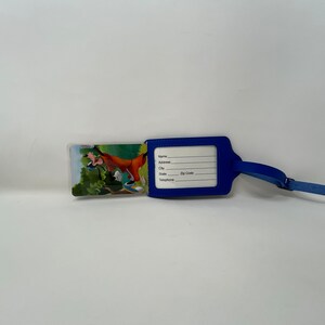 May include: Blue luggage tag featuring a cartoon image of Goofy on the front. The tag has a clear plastic window with spaces for name, address, city, state, postcode, and telephone number.