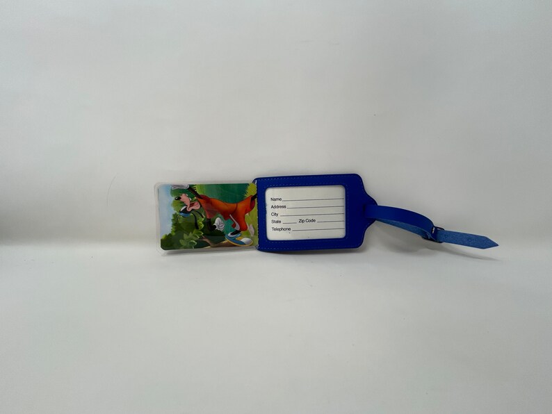 May include: Blue luggage tag featuring a cartoon image of Goofy on the front. The tag has a clear plastic window with spaces for name, address, city, state, postcode, and telephone number.