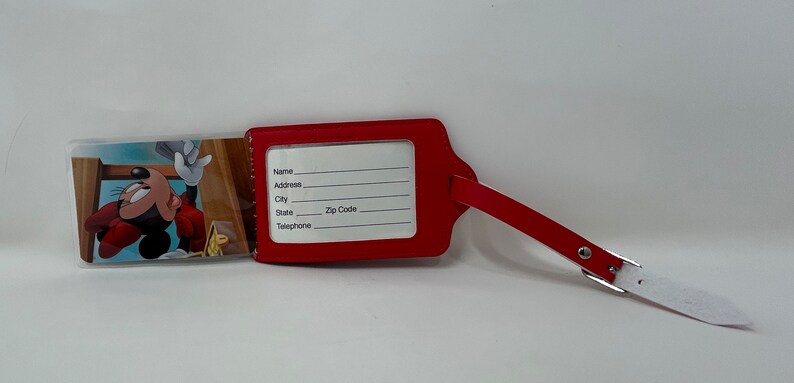 May include: Red luggage tag with a Mickey Mouse cartoon image on the front and a clear plastic window on the back with blank spaces for name, address, city, state, zip code, and telephone number.