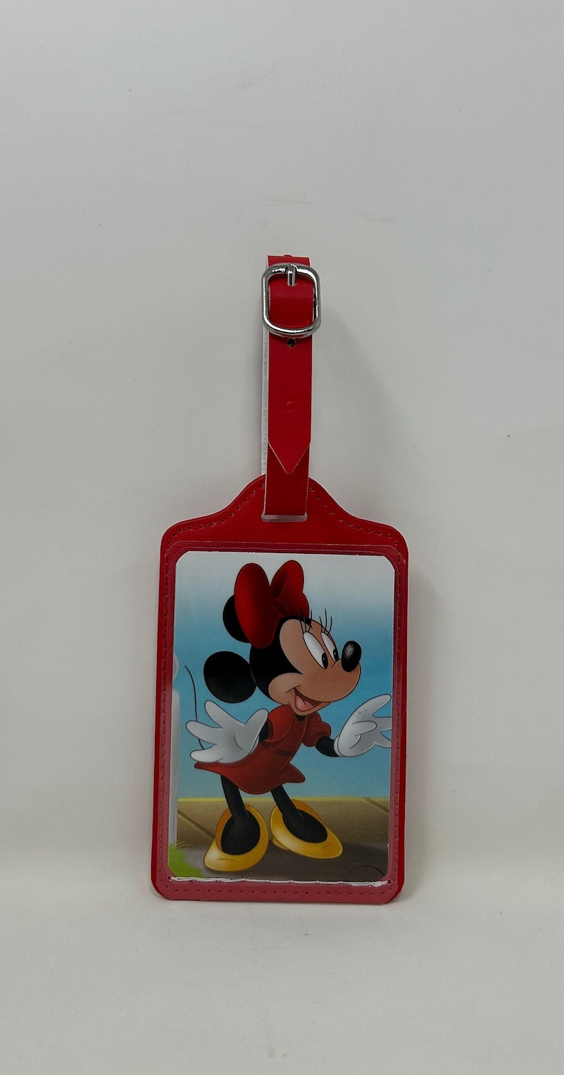 May include: Red leather luggage tag with a picture of Minnie Mouse in a red dress and yellow shoes. The tag has a silver buckle.
