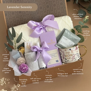 May include: A gift basket labeled "Lavender Serenity" contains a white knit blanket, purple ribbon, a floral mug, tea, chocolate, candles, socks, and an aromatic mist. The mug says "best MOM ever". The basket includes a gold-toned spoon and matches.