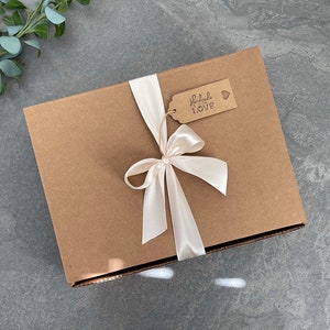 May include: A brown cardboard box with a white satin ribbon tied in a bow. The box has a small brown tag attached to the ribbon with the text "Handmade with LOVE" and a small heart.