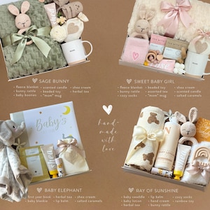 May include: Four gift boxes with baby-themed items. The boxes include blankets, toys, mugs, and skincare products. The text on the boxes reads "Sage Bunny", "Sweet Baby Girl", "Baby Elephant", and "Ray of Sunshine". The image also includes the text "hand made with love".
