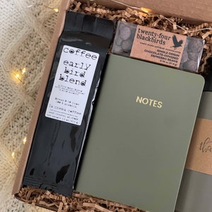 May include: A gift box filled with brown paper shreds contains a bag of coffee labeled "coffee early bird blend", a small box of chocolate covered espresso beans labeled "twenty-four blackbirds", a green notebook with the word "NOTES" in gold lettering, and a brown paper wrapped item with the word "thank" visible.