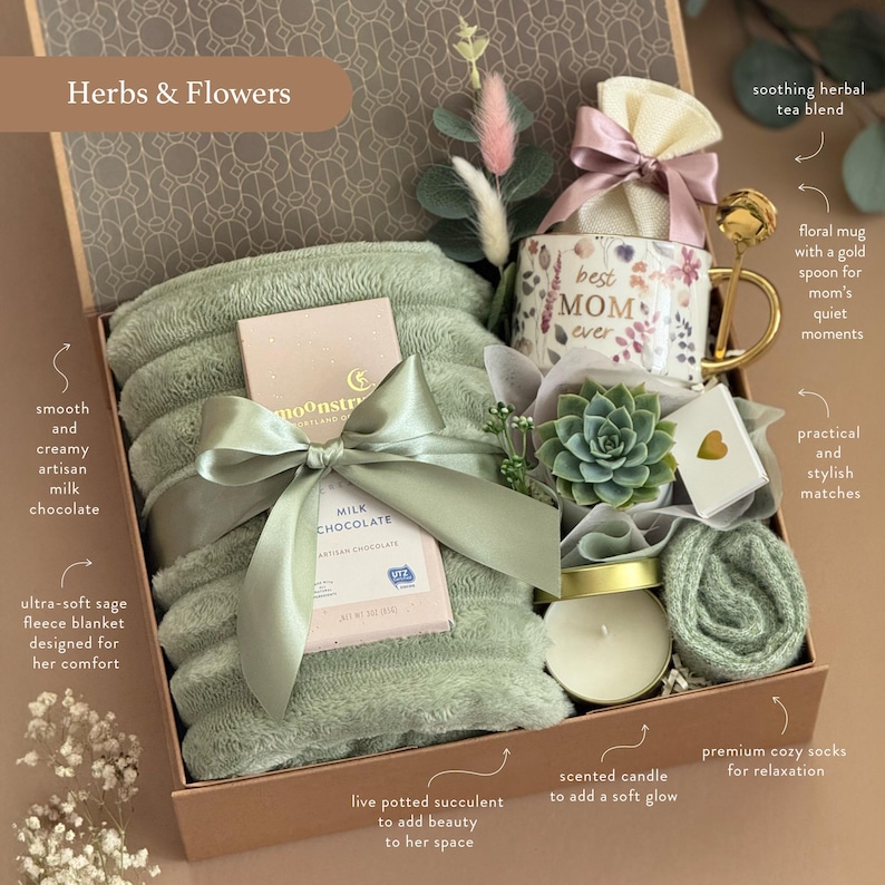 May include: A gift box with a sage green fleece blanket, a floral mug with "Best Mom Ever" text, a chocolate bar, a succulent, a candle, and cozy socks. The box is tied with a satin ribbon and includes a tea blend.