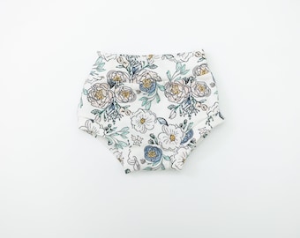 May include: White baby bloomers with a floral print featuring blue, green, and yellow flowers.