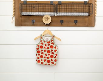 May include: A white tank top with a watermelon print. The tank top is hanging on a wooden hanger.