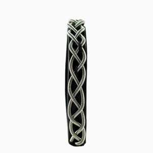 Può includere: Un braccialetto in pelle nera con un design intrecciato di corde di chitarra argentate.