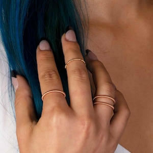 May include: A close-up of a hand wearing three thin gold rings. The rings are stacked on the ring finger.