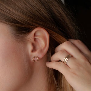 Puede incluir: Primer plano de la oreja de una persona con un pendiente de aro doble de oro. La persona lleva un anillo de oro y plata en el dedo.