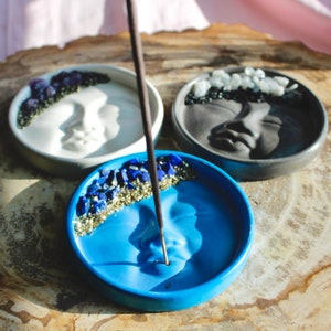 Pu&ograve; includere: Tre porta incensi in ceramica a forma di mezzaluna con volti. Ogni porta incensi &egrave; decorato con pietre preziose e glitter di diversi colori. Un bastoncino di incenso nero &egrave; posto nel porta incensi blu.
