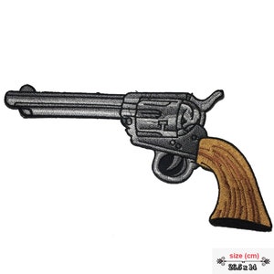 May include: An embroidered patch of a revolver with a wooden handle, in silver and brown. The patch measures 26.5 cm by 14 cm.