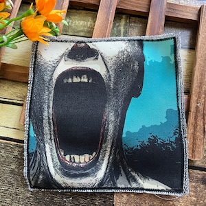 May include: A black and white patch featuring a graphic of a person's face with their mouth open in a scream. The background is a blue gradient with a dark silhouette of trees.