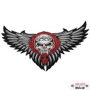 Könnte beinhalten: Gestickter Bügel-Patch mit einem weißen Totenkopf mit roten Augen und Zähnen, umgeben von einem roten Kranz und schwarzen Flügeln. Der Patch misst 27,5 cm x 15 cm.