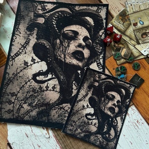 May include: Two fabric patches with a black and white Medusa illustration. The patches have a distressed, vintage look. The larger patch is rectangular, and the smaller one is square. The image also shows game pieces, including dice and cards.