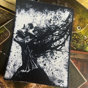 May include: Black and white graphic print of a skull with hair blowing in the wind. The print is on a black fabric background.
