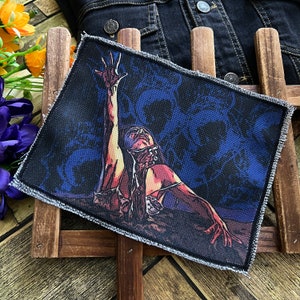 Könnte beinhalten: Ein gestickter Patch in Schwarz und Blau mit einer Frau, die die Arme nach oben ausstreckt. Die Frau ist von einem blauen und schwarzen Blumenmuster umgeben.