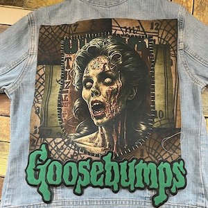 Könnte beinhalten: Eine blaue Jeansjacke mit einem grünen Goosebumps-Patch und einem Grafikdruck einer Zombiefrau auf der Rückseite.