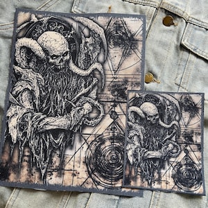 May include: Two black and white embroidered patches featuring a demonic figure with horns and tentacles. The patches are set against a background of geometric shapes and swirling patterns.