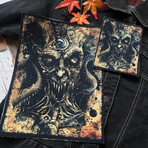 May include: Two embroidered patches featuring a detailed illustration of a monstrous creature with a single eye and tentacles. The creature has a menacing expression with sharp teeth and a dark, textured background.