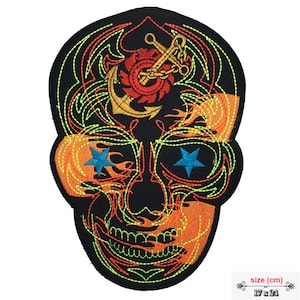 May include: Embroidered iron-on patch featuring a black skull with flames, an anchor, and stars. The skull is outlined in green and orange thread. The patch measures 17 x 24 cm.