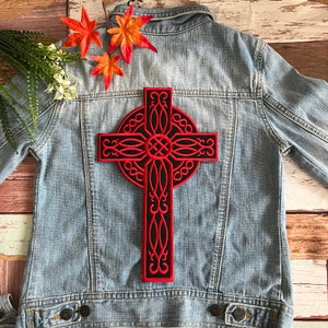 May include: A red and black Celtic cross patch with intricate details. The patch is ironed onto a blue denim jacket.