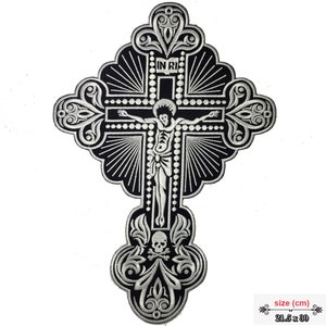 Könnte beinhalten: Ein schwarzer und silberner gestickter Bügeleisen-Aufnäher mit einem Kruzifix mit Totenkopf und Knochen am unteren Ende. Der Aufnäher ist 21,5 cm x 30 cm groß. Der Text "IN RI" ist auf dem Kreuz sichtbar.