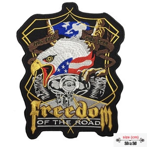 Könnte beinhalten: Ein schwarzer und goldener gestickter Patch mit einem amerikanischen Weißkopfseeadler, der einen Motorradmotor hält. Der Adler hält eine amerikanische Flagge und der Text "True Free True Ride" befindet sich auf einem Banner über dem Adler. Der Text "Freedom of the Road" befindet sich unter dem Motor. Der Patch ist 20 x 25 cm groß.