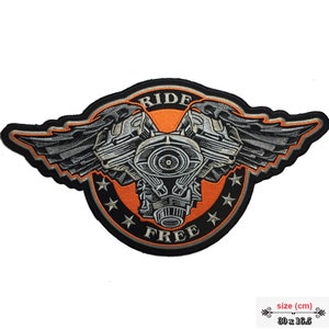Op de afbeelding: Gestikt motorfiets patch met een zilveren motorontwerp, vleugels en de woorden "Ride Free" in een zwarte cirkel met een oranje achtergrond. De patch is 30 x 16,5 cm.