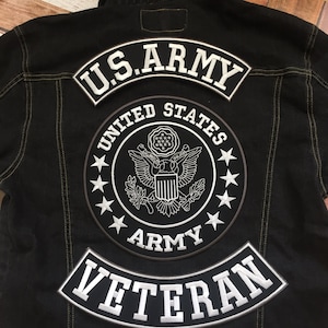 May include: A black denim jacket with three embroidered patches. The top patch says "U.S. ARMY" in white lettering. The middle patch is a circular patch with a white eagle and shield design and the words "UNITED STATES ARMY". The bottom patch is a curved patch that says "VETERAN" in white lettering.