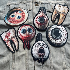 May include: Seven embroidered iron-on patches with a horror theme. The patches feature a bloody eyeball, a bloody tooth, a bowl of eyeballs, a screaming face, and three different bloody eyeballs.
