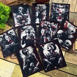 Könnte beinhalten: Eine Sammlung rechteckiger Aufnäher mit gotischen Illustrationen. Die Aufnäher zeigen Bilder von Schädeln, Figuren und blutartigen Spritzern in Schwarz, Weiß und Rot. Die Aufnäher sind auf einer Holzoberfläche angeordnet.