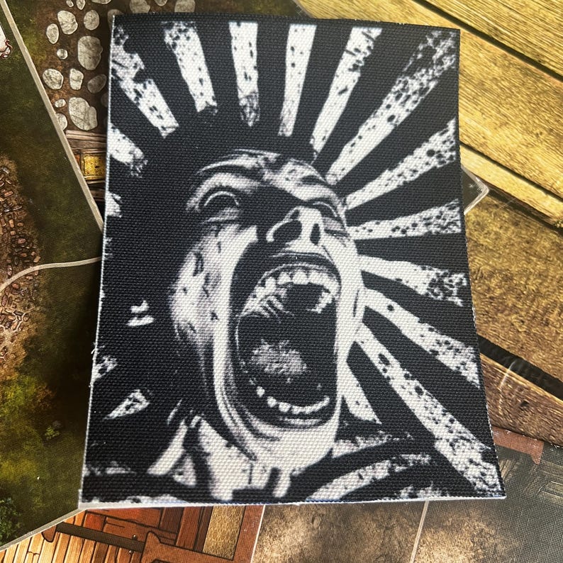 May include: Black and white patch featuring a graphic of a person screaming with their mouth open. The background is a black and white sunburst pattern.