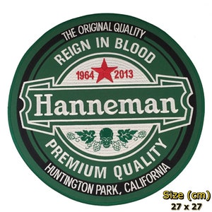 Op de afbeelding: Een ronde groene en zwarte patch met witte borduursels. De patch heeft de tekst "The Original Quality", "Reign in Blood", "1964 2013", "Hanneman", "Premium Quality" en "Huntington Park, California". Een rode ster en een schedel met bladeren zijn ook geborduurd op de patch. De patch meet 27 cm bij 27 cm.