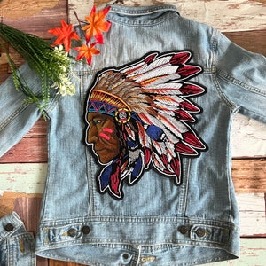 Può includere: Una giacca di jeans con una toppa ricamata colorata di un capo nativo americano che indossa un copricapo con piume. La toppa è sul retro della giacca.