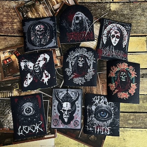 May include: Ten black and white iron-on patches with various graphic designs. The patches feature skulls, eyes, and other spooky imagery. The patches are all rectangular and have a distressed, vintage look. The text on the patches includes "WANTED", "LOOK", "THERE", and "SHROOM QUEENS".