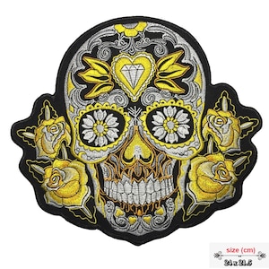 May include: A black and white embroidered sugar skull with yellow roses and a diamond in the forehead. The skull is 24 x 21.5 cm.