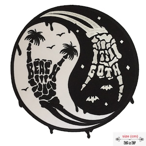 May include: Black and white yin yang symbol with a skeleton hand forming the shape of a peace sign on the white side and the words "Beach Goth" on the black side. The symbol is dripping with black and white paint.