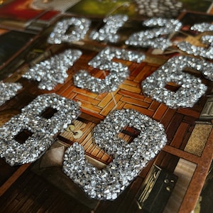 Peut inclure: Gros plan sur un ensemble de chiffres en paillettes argentées, de 1 à 9, disposés de manière aléatoire sur une surface en bois.