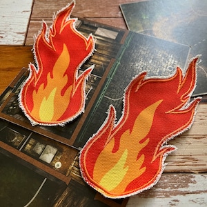 Peut inclure: Deux patchs en tissu de flamme rouge et jaune avec des coutures blanches autour des bords. Les flammes sont stylisées et ont un effet 3D.
