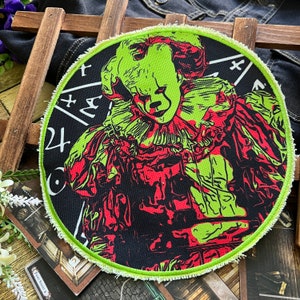 Op de afbeelding: Een geborduurde zwarte en groene patch met een clown in een rood en groen kostuum. De clown is omringd door een zwart-wit patroon van wiskundige symbolen. De patch heeft een rafelige rand.