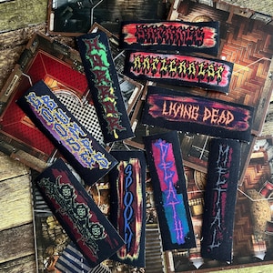Könnte beinhalten: Eine Sammlung von neun bunten Stoff-Patches mit verschiedenen Bandnamen, darunter "Spook", "Living Dead", "Death" und "Metal".