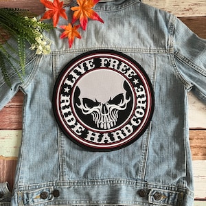 Può includere: Una toppa ricamata in bianco e nero con un teschio e il testo "Ride Free Live Hardcore" su una giacca di jeans.