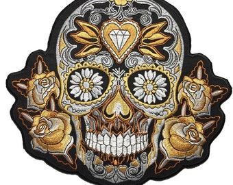 Puede incluir: Parche de hierro bordado con un cráneo de azúcar negro y blanco con detalles dorados. El cráneo tiene un diamante en forma de corazón en la frente, diseños florales alrededor de los ojos y rosas en los lados. El parche mide 24 x 21,5 cm.