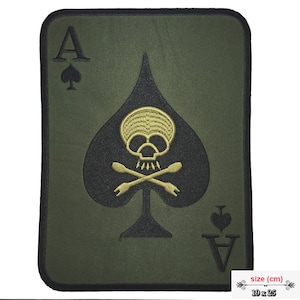 May include: A rectangular Ace of Spades patch with a skull and crossbones design. The patch has rounded corners, a black spade on a green background, and a gold skull. The patch measures 19 x 25 cm.