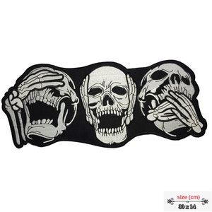 May include: Three embroidered skulls, each with a different hand gesture: one covering its eyes, one covering its ears, and one covering its mouth. The skulls are white and the background is black. The patch measures 30 x 14 cm.