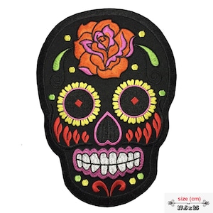 Könnte beinhalten: Schwarzer gestickter Bügel-Patch mit einem Zucker-Schädel mit einer rosa und orangefarbenen Rose auf der Stirn, gelben und rosa floralen Details und einem weißen Lächeln. Der Patch misst 17,5 cm x 25 cm.